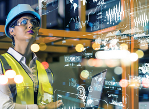 Kvinne i industrielt miljø med vernehjelm og refleksvest ser på digitale data og grafer som svever foran henne. Bildet illustrerer smart produksjon og datadrevet industri.