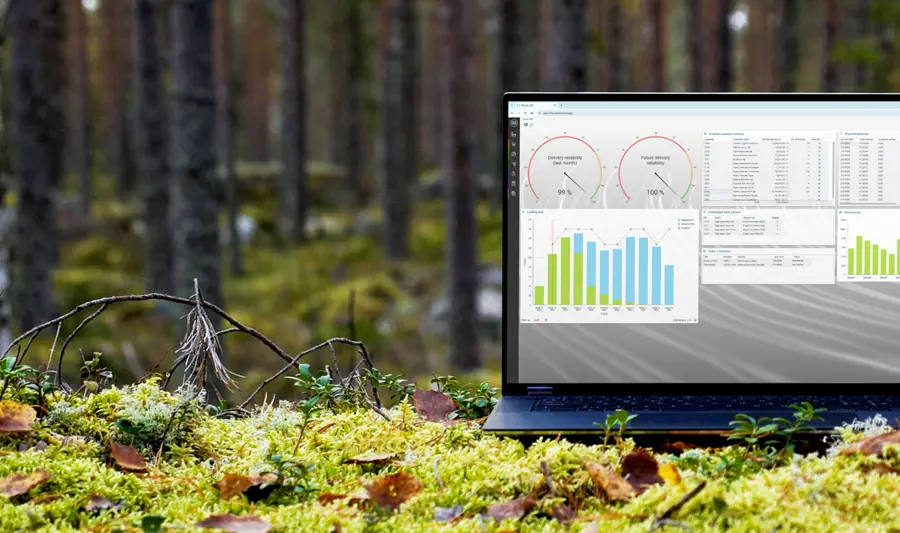 A laptop computer displaying Monitor ERP sitting on top of a moss covered ground surrounded by trees.