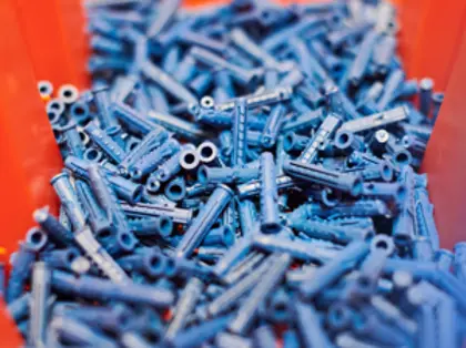 Plastikowe kołki uzyskane z produkcji tworzyw sztucznych w czerwonym pojemniku.