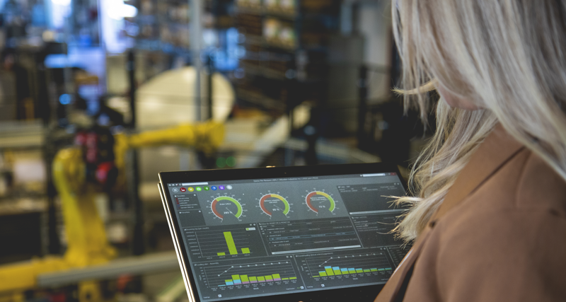 A person holding a tablet computer in a factory environment displaying Monitor ERP dashboard. 