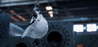 A white helmet hanging from a hook in a factory.