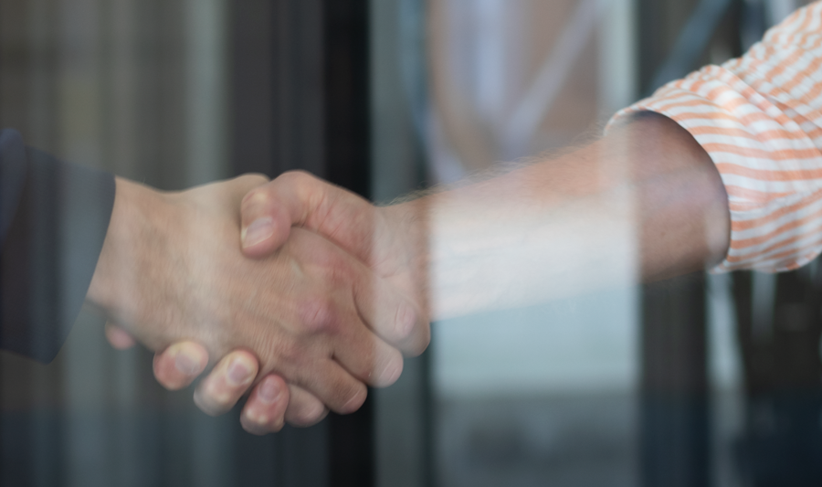 Two people shaking hands in front of a glass door.