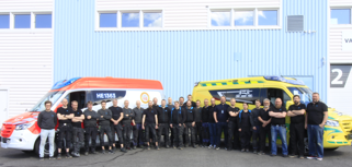 En grupp människor står framför två bilar.