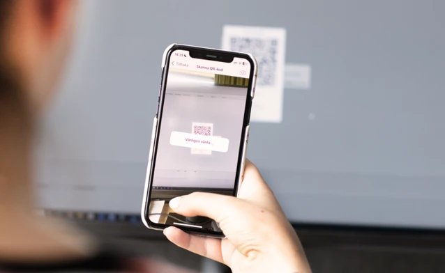 A person holding a cell phone in their hand scanning a qr code on a computer screeen.