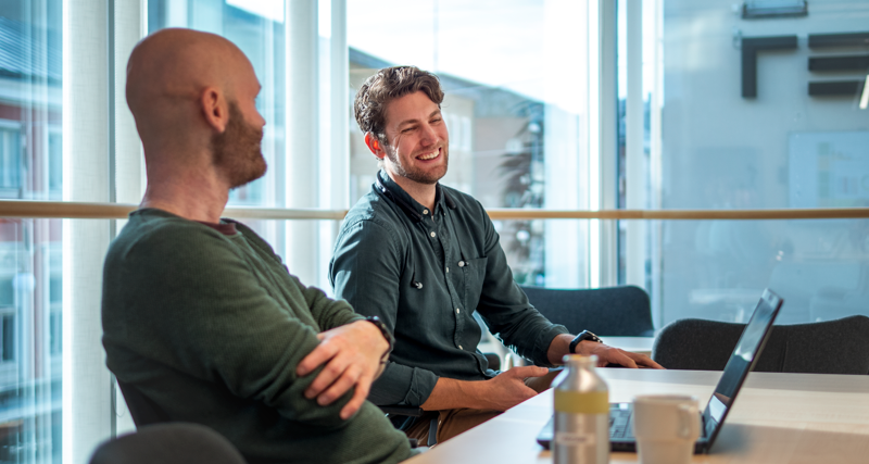 Ett par män som sitter vid ett bord med bärbara datorer.