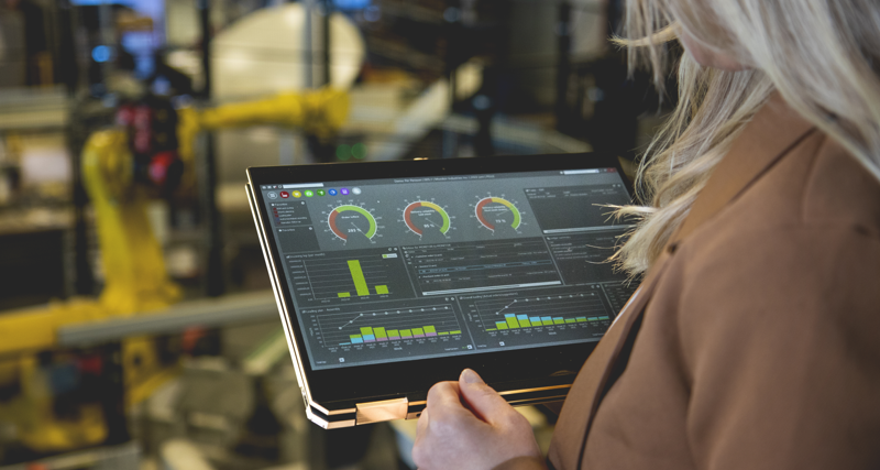 A person holding a tablet computer in a factory environment displaying Monitor ERP dashboard. 