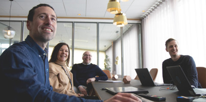 A group of people sitting around a table with laptops in a conference room. 