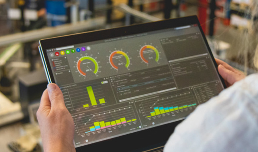 A person holding a tablet computer in a factory environment displaying Monitor ERP dashboard. 
