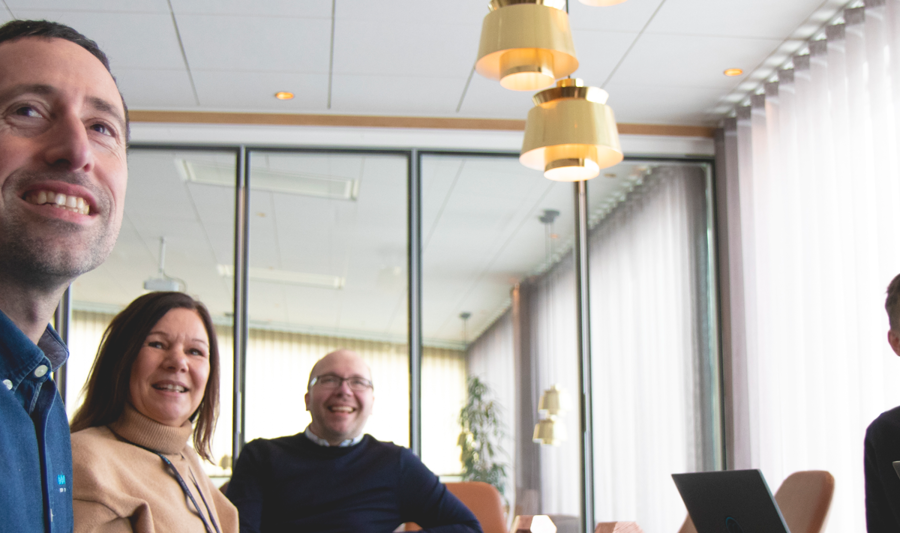 A group of people sitting around a table with laptops in a conference room. 