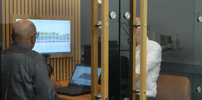 A man standing in front of a laptop computer displaying Monitor ERP dashboards. 