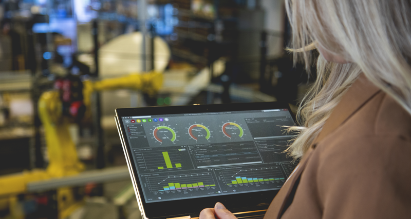 A person holding a tablet computer in a factory environment displaying Monitor ERP dashboard. 