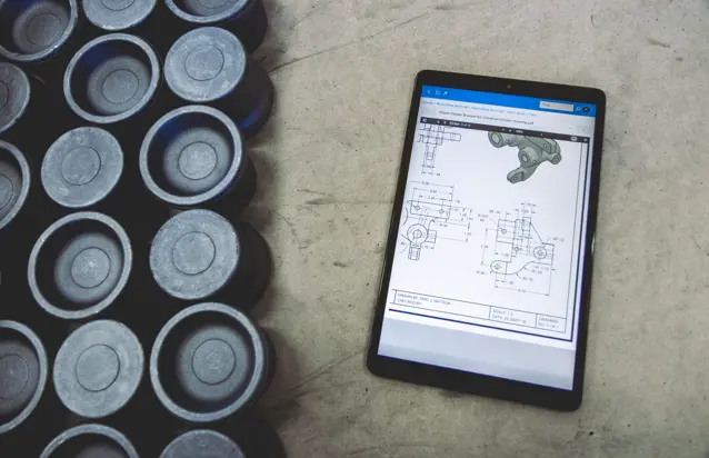 Tablet z uruchomionym systemem Monitor ERP, wyświetlającym rysunek techniczny - w tle gumowe elementy poprodukcyjne.