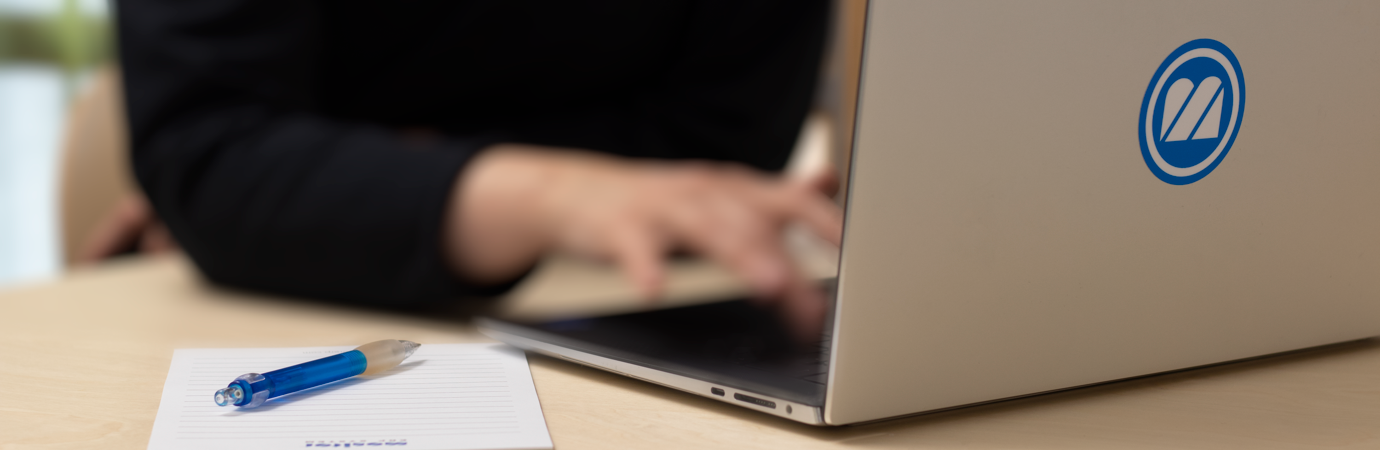 A person typing on a laptop with a pen.