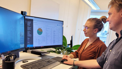 Two people are standing in front of a computer, where one is demonstrating and explaining how the Monitor ERP system works to the other.