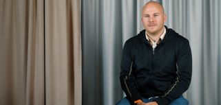 A man sitting on a chair in front of a curtain.