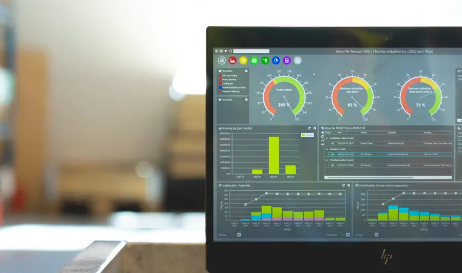 Laptop z uruchomionym systemem Monitor ERP, stojący na stoliku w magazynie firmy produkcyjnej.