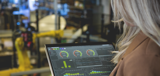 En person som håller i en surfplatta i en fabriks­miljö och visar Monitor ERP:s instrumentpanel.