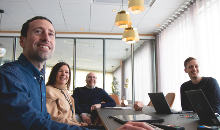 A group of people sitting around a table with laptops in a conference room. 