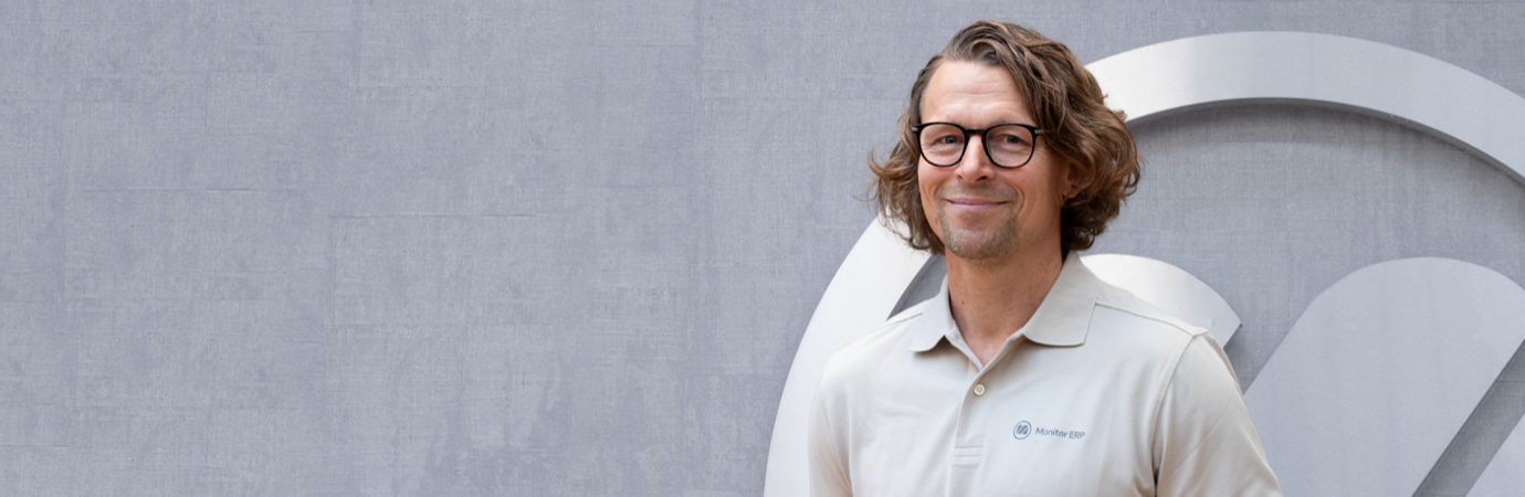 A man with glasses standing in front of a wall.