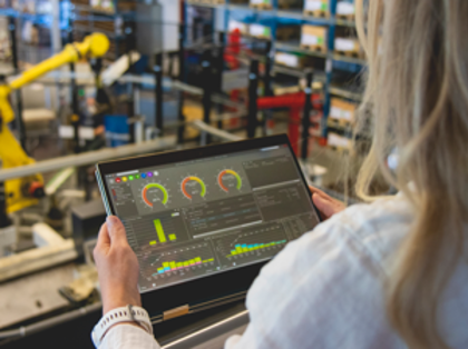 En person som håller en surfplatta i en fabriksomgivning, med Monitor ERP-dashboarden visad på skärmen.