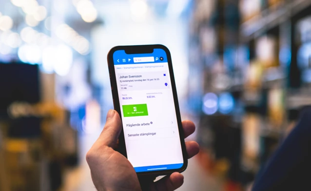A person in a warehouse holding a cellphone displaying Monitor Mobile.
