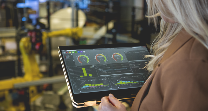 A person holding a tablet computer in a factory environment displaying Monitor ERP dashboard. 