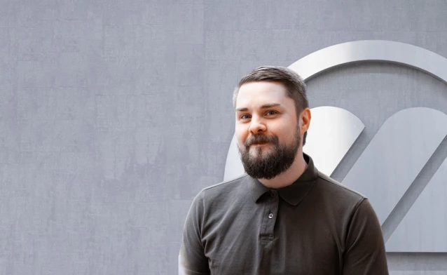 A man with a beard standing in front of a logo.
