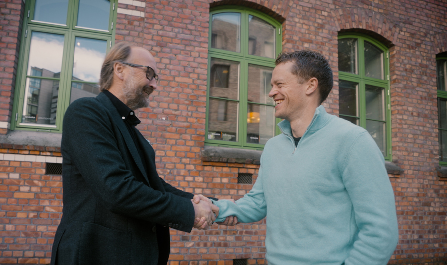 To menn håndhilser foran en murbygning, begge smiler og ser ut til å ha en hyggelig samtale. Monitor ERP-logoen er synlig øverst i venstre hjørne.