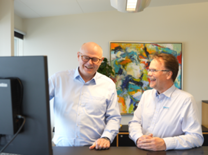 Two men standing in front of a computer looking at Monitor ERP looking happy.