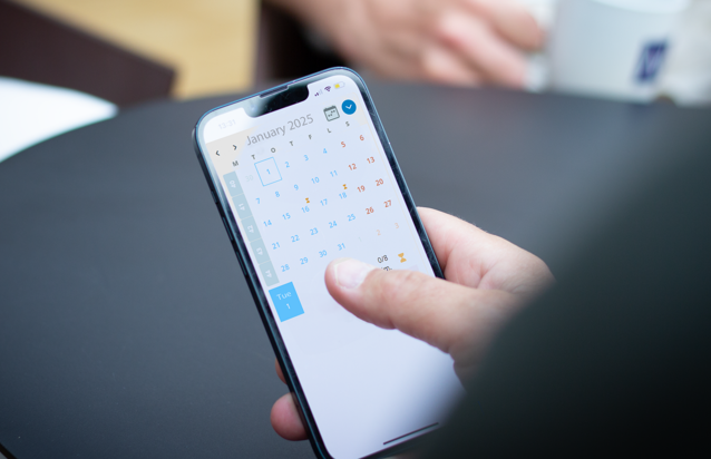 A person holding a cell phone with a calendar on the screen.