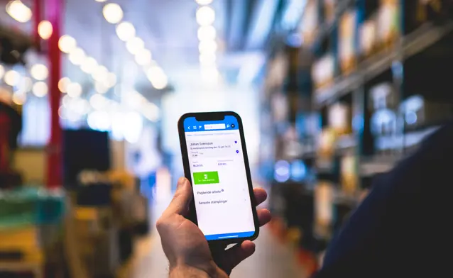 A person in a warehouse holding a cellphone displaying Monitor Mobile.