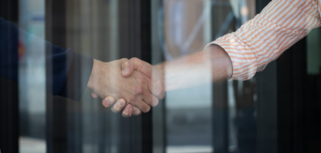 Two people shaking hands in front of a glass door.