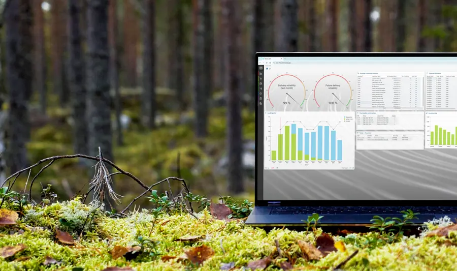 A laptop computer displaying Monitor ERP sitting on top of a moss covered ground surrounded by trees.