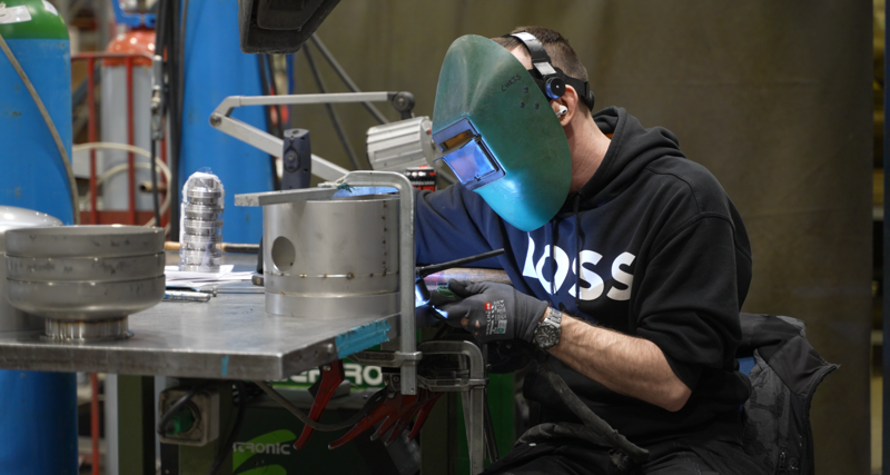 A person is welding in a factory. They are wearing a welding helmet.