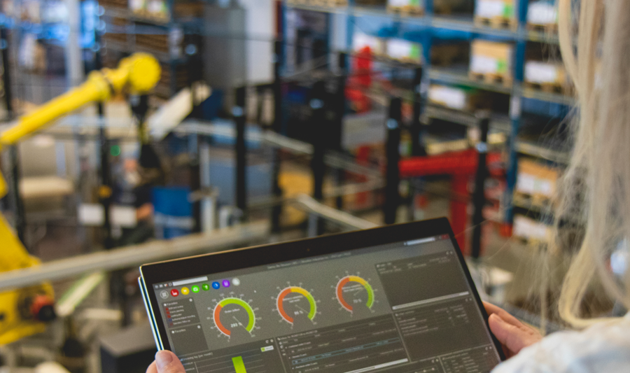 En person håller i en surfplatta i en fabriksmiljö som visar Monitor ERP:s instrumentpanel.