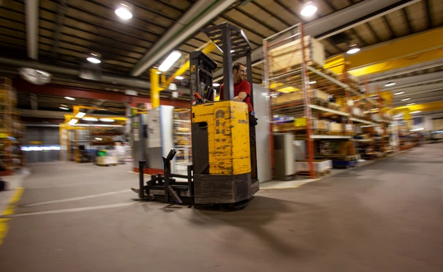A forklift in a large warehouse with lights on.