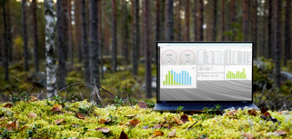 A laptop computer with Monitor ERP dashboard (sustainability functions) sitting on top of a moss covered field.