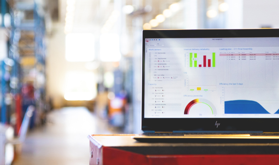 Bærbar PC med visning av dataanalyse og grafer, plassert på en arbeidsbenk i en moderne industribygning eller fabrikk.