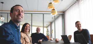 A group of people sitting around a table with laptops in a conference room. 