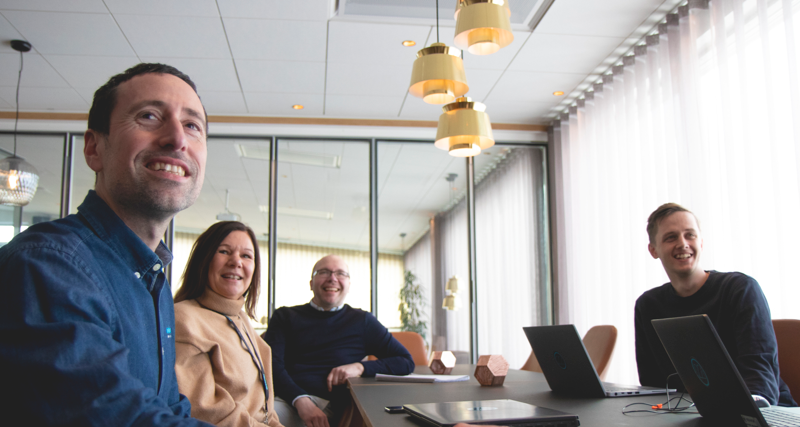 A group of people sitting around a table with laptops in a conference room. 