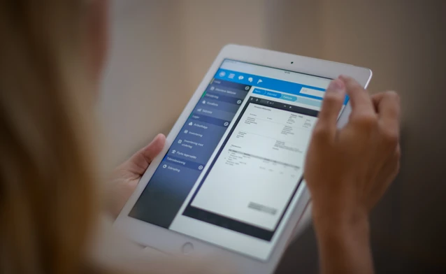 A woman is holding a tablet displaying a digital invoice. 