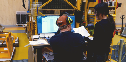 Two people standing in a warehous, looking at a computer with a Monitor ERP dashboard. 