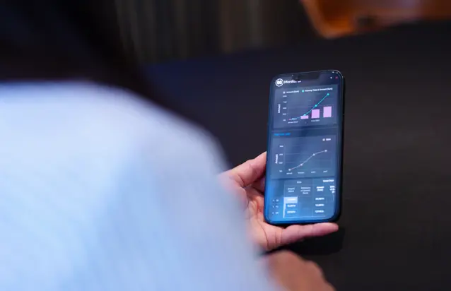 Osoba trzymająca smartfon z ekranem danych systemu Monitor ERP i Monitor BI.