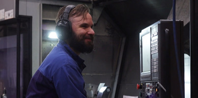 A man in a blue shirt and headphones working on a machine.