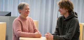 Petra Fahje and Fynn Höfer, support specialists, standing next to a table and talking to each other. 