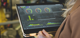 A person holding a tablet computer in a factory environment displaying Monitor ERP dashboard. 