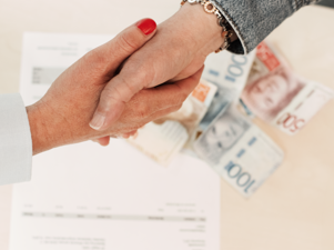 A handshake between two people. A contract and some money is laying on the table.