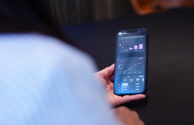 En person håller en mobiltelefon som visar dashboards från Monitor ERP.