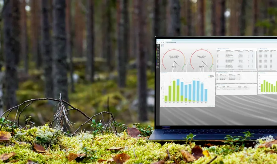 A laptop computer displaying Monitor ERP sitting on top of a moss covered ground surrounded by trees.