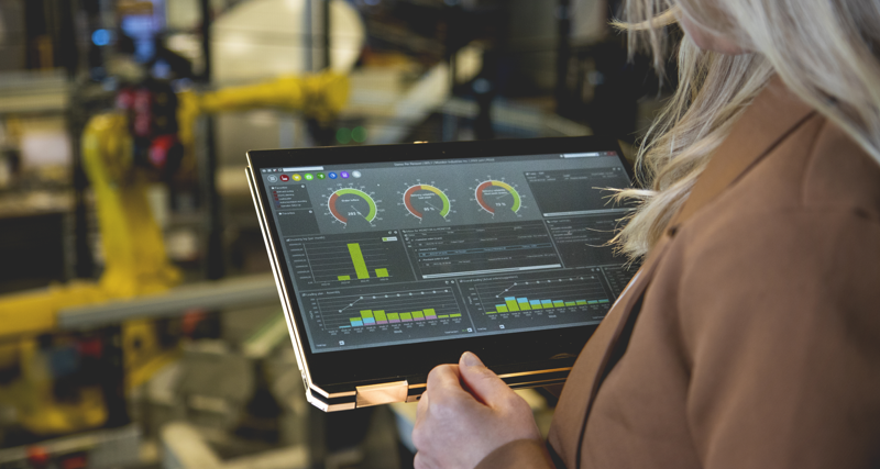 A person holding a tablet computer in a factory environment displaying Monitor ERP dashboard. 